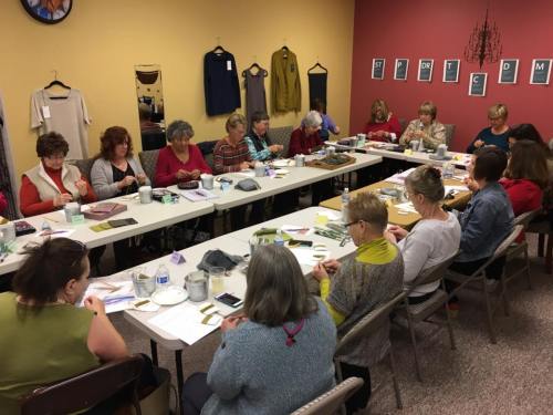 A group of people seated at tables, engaged in a crafting workshop in a cozy, colorful room.