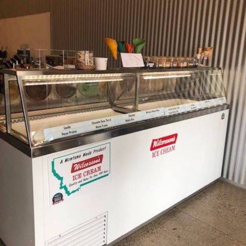 A display case filled with various ice cream flavors and colorful cones in a shop setting.
