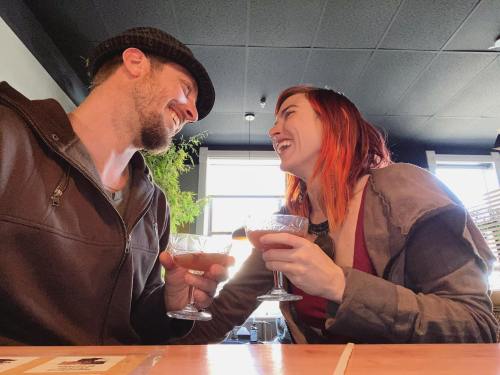 A couple smiles at each other while toasting with cocktails in a cozy restaurant setting.