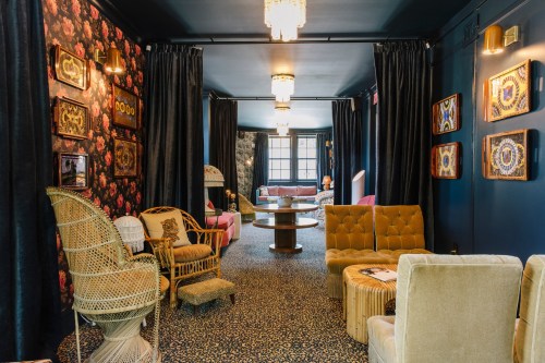 A stylish lounge with floral wallpaper, plush seating, and decorative art, creating a cozy and inviting atmosphere.