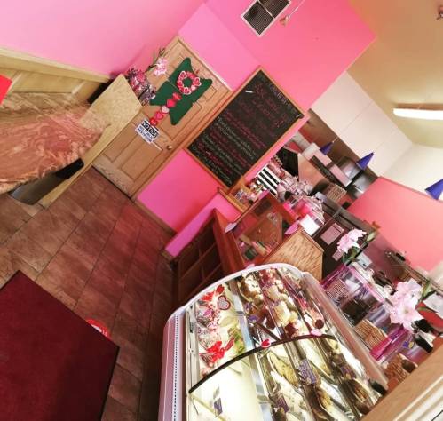 A colorful bakery interior with pink walls, a display case of treats, and a chalkboard menu in the background.