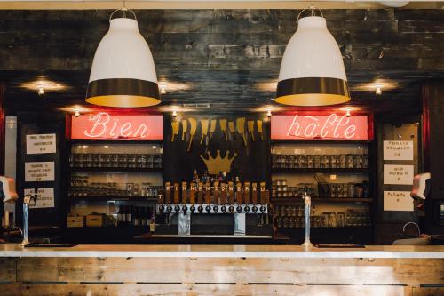 A cozy bar with a wooden counter, illuminated signs reading "Bier" and "Halle," and a variety of beer taps and glasses.