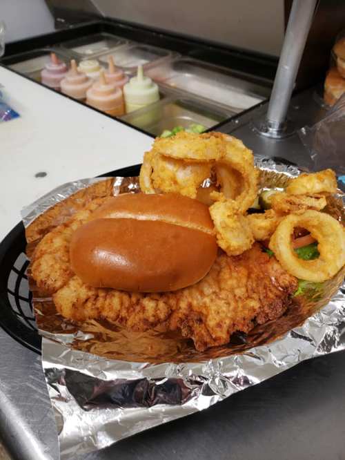 A basket with a fried chicken sandwich, onion rings, and a side of lettuce, on a foil-lined tray.