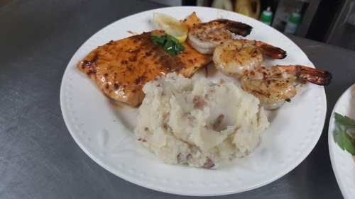 A plate featuring grilled salmon, shrimp, and creamy mashed potatoes, garnished with a lemon wedge and parsley.