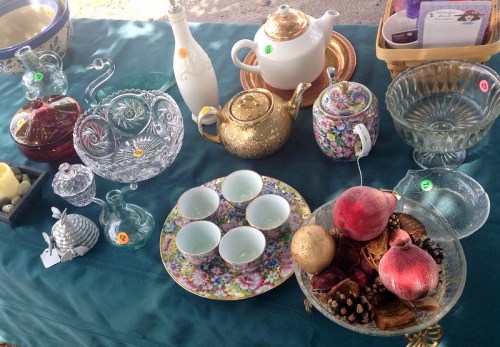 A variety of vintage items including glassware, teapots, and decorative bowls displayed on a green tablecloth.