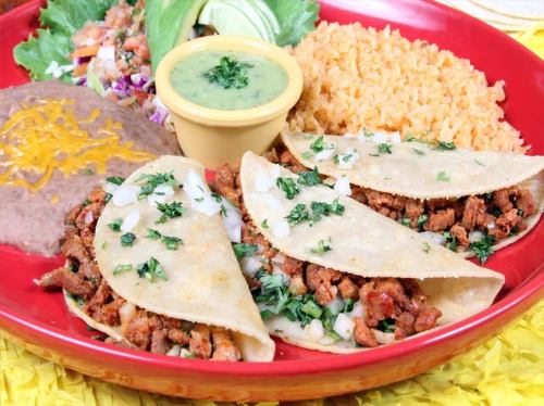 A vibrant plate of tacos with meat, onions, and cilantro, served with rice, refried beans, and green sauce.