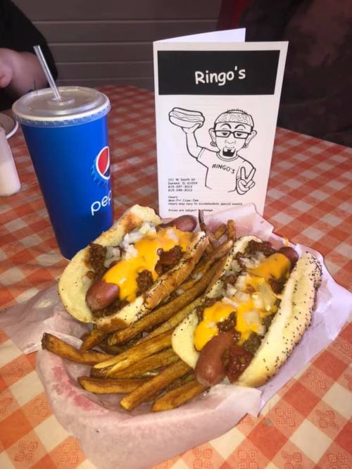 Two loaded hot dogs with cheese and onions, served with crispy fries and a Pepsi, alongside a menu featuring a cartoon character.