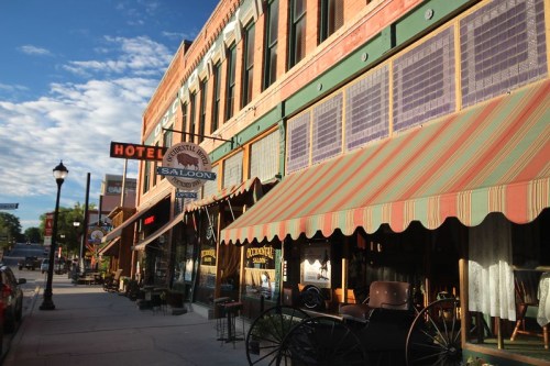 Historic buildings line a street, featuring a hotel and saloon with colorful awnings and vintage decor.