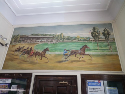 A mural depicting a horse race with jockeys, set against a backdrop of a racetrack and spectators.