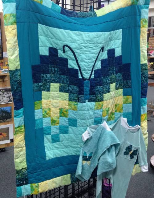 A turquoise quilt featuring a butterfly design, displayed alongside matching children's clothing.
