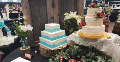 A display of two elegant wedding cakes with floral decorations, surrounded by greenery and candles on a rustic table.