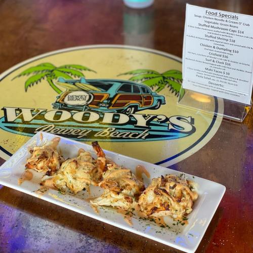 A plate of stuffed crab cakes on a table with a menu for Woody's Dewey Beach.