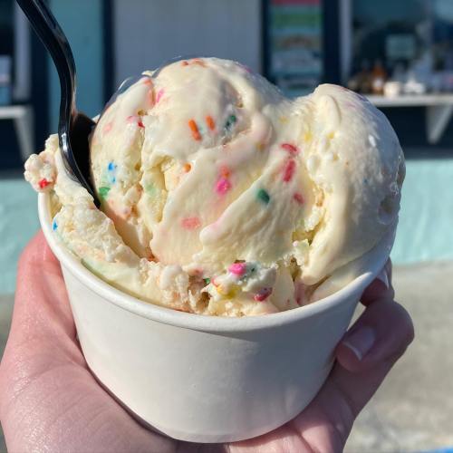 A hand holding a cup of colorful sprinkles ice cream on a sunny day.