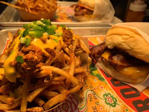 A plate of loaded fries topped with cheese and green onions, alongside a burger with bacon on a colorful tray.