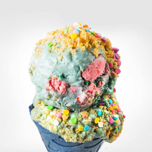A colorful ice cream cone topped with blue and pink scoops, sprinkled with colorful candy and crumbs.