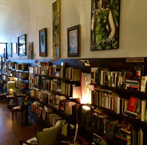 A cozy library with wooden shelves filled with books, framed artwork on the walls, and comfortable seating.