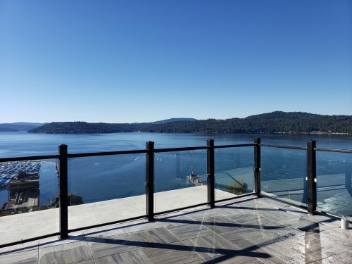 A clear blue lake view from a balcony, surrounded by green hills under a bright blue sky.