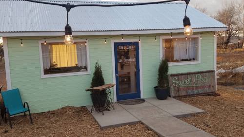 A small green building with a blue door, string lights, and a sign reading "Sweet Pea Farm & Orchard."