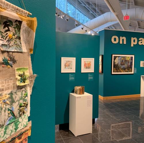 Art gallery interior featuring colorful walls, framed artwork, and a textile piece on display.