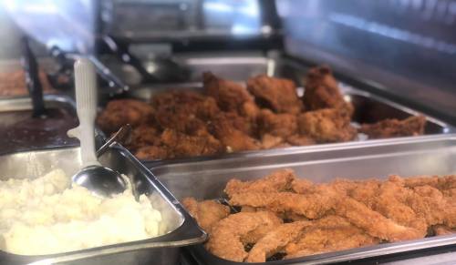 A serving station with trays of fried chicken, crispy strips, and mashed potatoes.