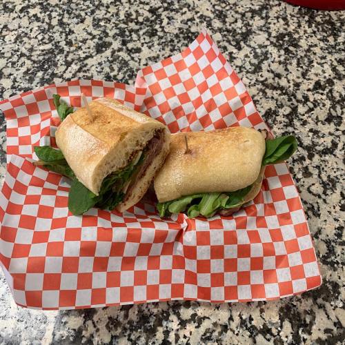 Two sandwiches with fresh greens, placed on a red and white checkered paper on a speckled countertop.