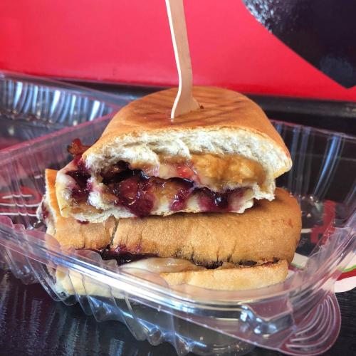 A sandwich with layers of peanut butter and jelly, served in a clear plastic container with a wooden stick.