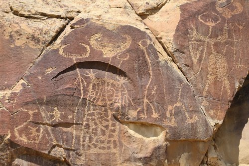 Petroglyphs on a rock surface, depicting abstract figures and symbols in earthy tones.