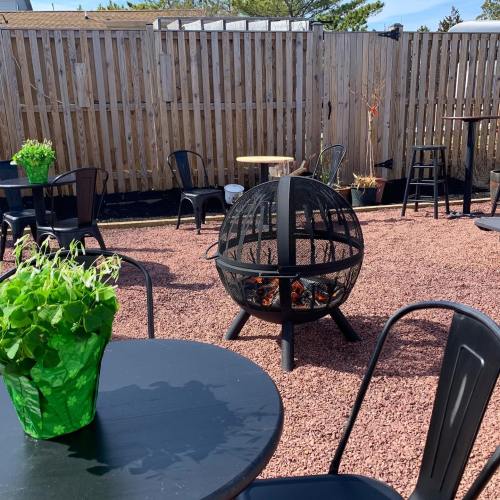 A cozy outdoor space with a fire pit, black tables, and green plants, surrounded by a wooden fence.