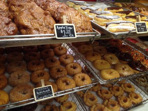 A display of various donuts and pastries, including apple fritters, cream-filled bars, and seasonal options.