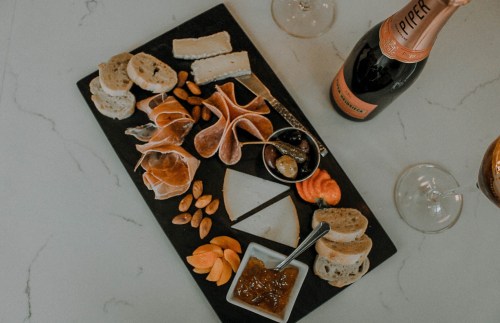 A charcuterie board with cheeses, meats, nuts, fruit, and a bottle of champagne, set on a marble surface.