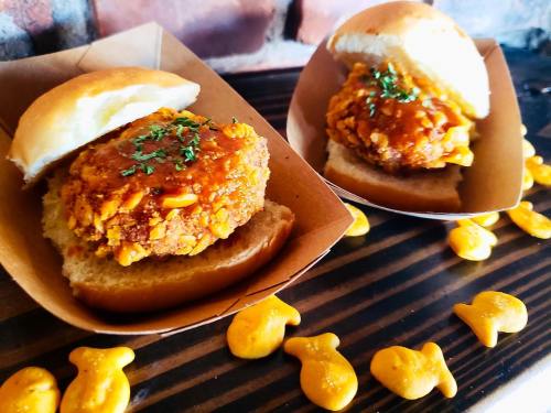 Two sliders with crispy chicken patties topped with sauce, served in soft buns, surrounded by goldfish crackers.