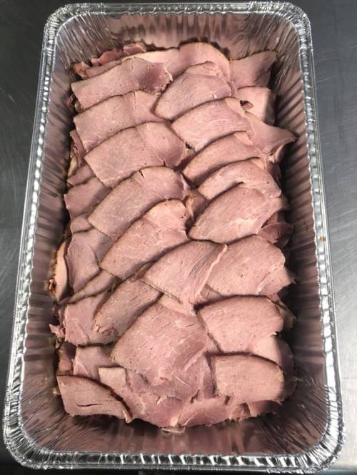 A tray filled with neatly arranged slices of cooked meat, showcasing a layered presentation.
