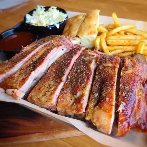 A plate of smoked ribs with a side of coleslaw, fries, and a piece of bread, served with barbecue sauce.