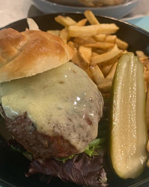 A juicy burger with melted cheese, served with fries and a pickle on the side, all on a black plate.