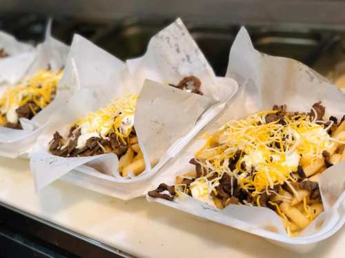 Four trays of loaded fries topped with seasoned beef, shredded cheese, and sour cream, served in paper liners.