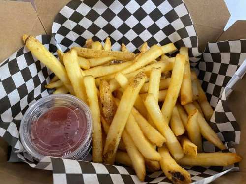 A box of golden French fries with a small container of ketchup on a checkered paper lining.