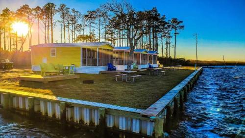 Colorful cabins by the water at sunset, surrounded by trees and a gentle wave lapping at the dock.