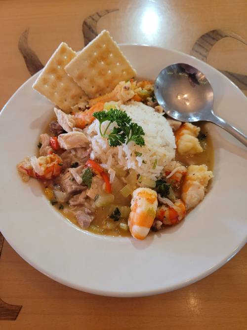 A plate of seafood stew with rice, shrimp, chicken, and vegetables, garnished with parsley and served with crackers.