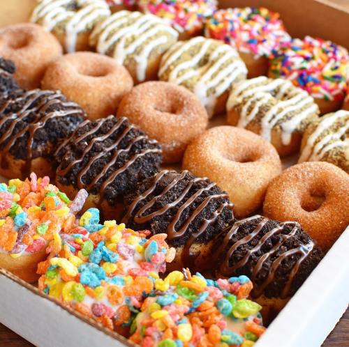 A box of assorted donuts, featuring chocolate, sprinkles, and colorful cereal toppings.