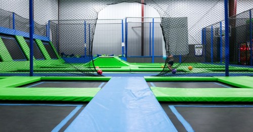 A spacious indoor trampoline park with green and blue trampolines surrounded by safety nets.