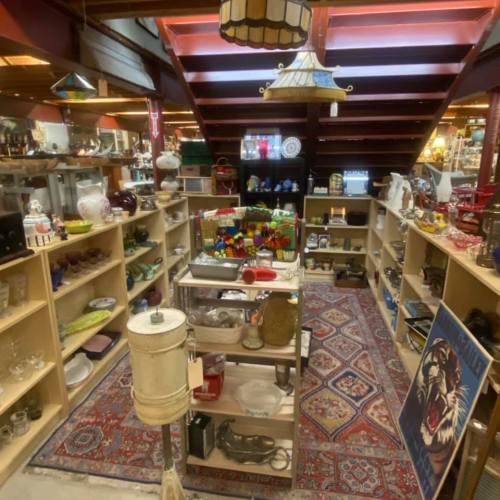 A cozy antique shop filled with various vintage items, shelves lined with collectibles, and a colorful rug on the floor.