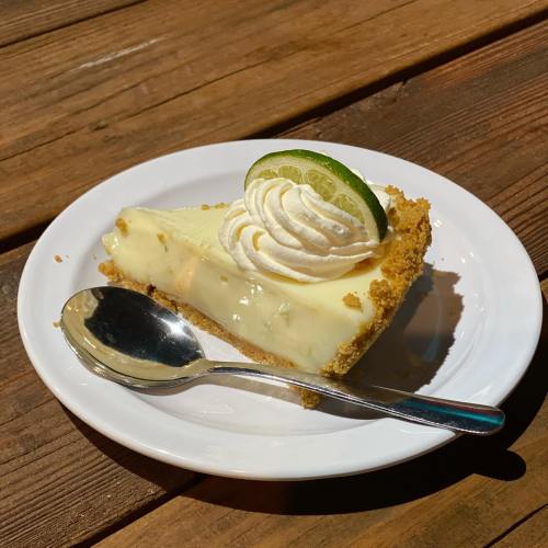 A slice of key lime pie topped with whipped cream and a lime wedge, served on a white plate with a spoon.