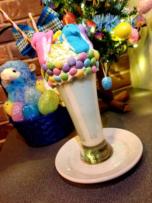 A colorful milkshake topped with whipped cream, pastel candies, and marshmallows, set against a festive background.