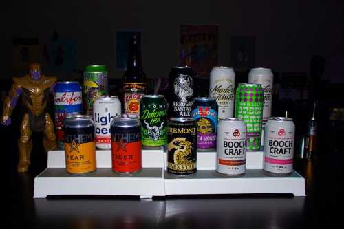 A variety of colorful beer and cider cans displayed on a shelf, with a toy figure in the foreground.