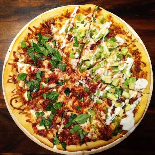 A pizza divided into two halves: one topped with herbs and meat, the other with avocado and drizzled with sauce.