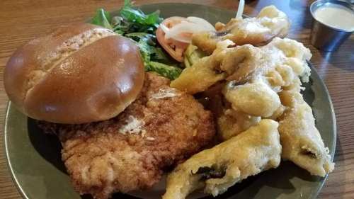 A plate featuring a fried chicken sandwich, lettuce, tomato, and a side of fried vegetables.