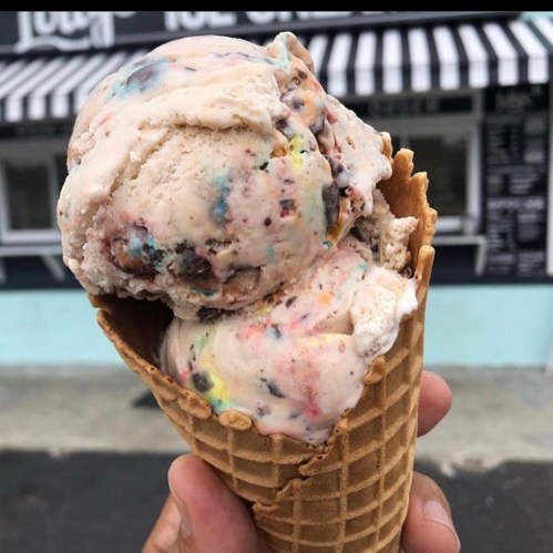 A hand holding a waffle cone filled with two scoops of colorful ice cream.