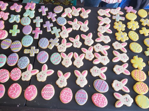 A colorful assortment of decorated cookies shaped like bunnies, eggs, and flowers, arranged on a black table.