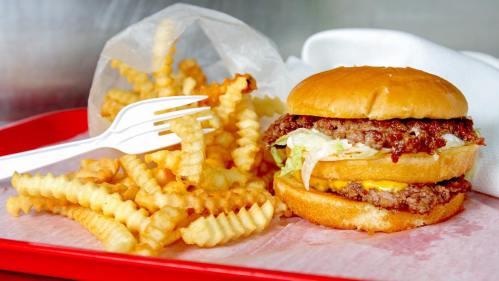 A juicy burger with lettuce and cheese next to a serving of crinkle-cut fries on a red tray.