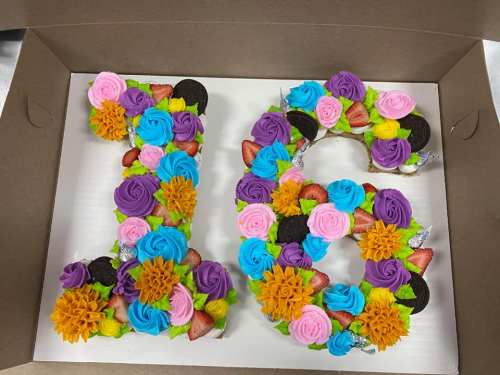 Colorful cake shaped like the numbers 1 and 6, decorated with flowers, strawberries, and cookies.